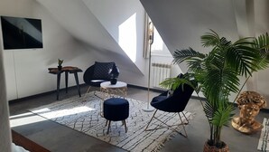 Um quarto moderno estilo loft, com teto inclinado, uma janela grande, uma poltrona de couro preto, uma mesa de centro redonda e um vaso de plantas.