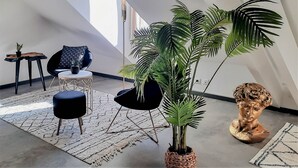 Um loft moderno com teto alto, uma planta grande em vaso, uma cadeira preta, uma mesinha com planta e um busto escultural.