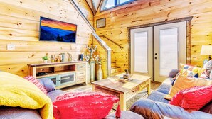L’intérieur d’un chalet confortable, avec des murs en bois, un banc en bois, un canapé, une table basse et un téléviseur fixé au mur.