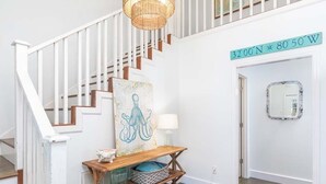 Eine Treppe mit weißen Geländern, ein Holztischchen mit Körben, ein dekoratives Wandelement und ein Spiegel.