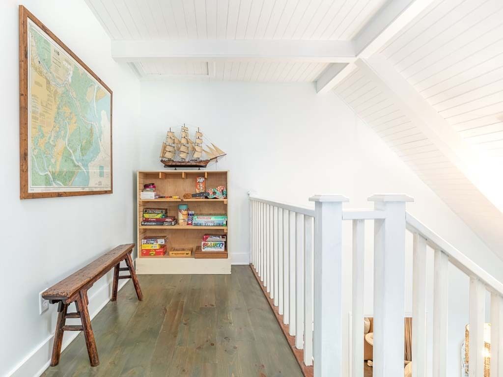 Un pasillo estrecho con un banco de madera, una estantería con juguetes, un mapa y una barandilla blanca.