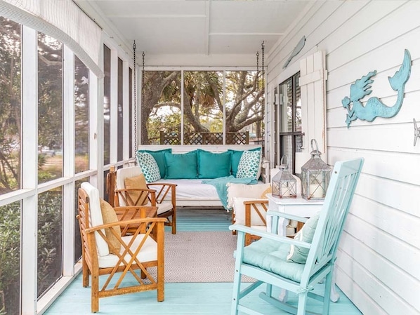 A porch with wicker chairs, a swing, and a table.