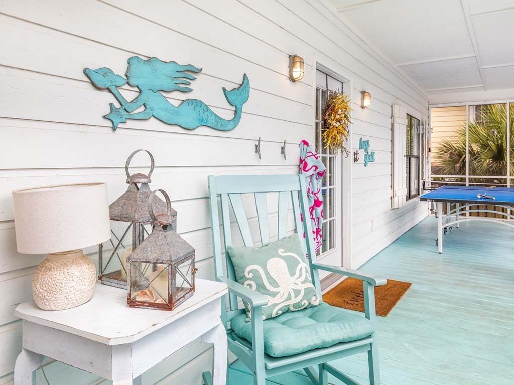 A room with a teal chair, a white table with a lamp, and a decorative wall piece.