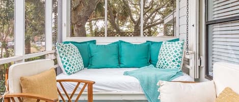 A porch with a swing, wooden chairs, and a white sofa with teal cushions.