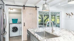A modern kitchen with a large sink, a washing machine, and a sliding door leading to a patio. - Lucky Charm by Tybee Vacation Rentals (Tybee Island)