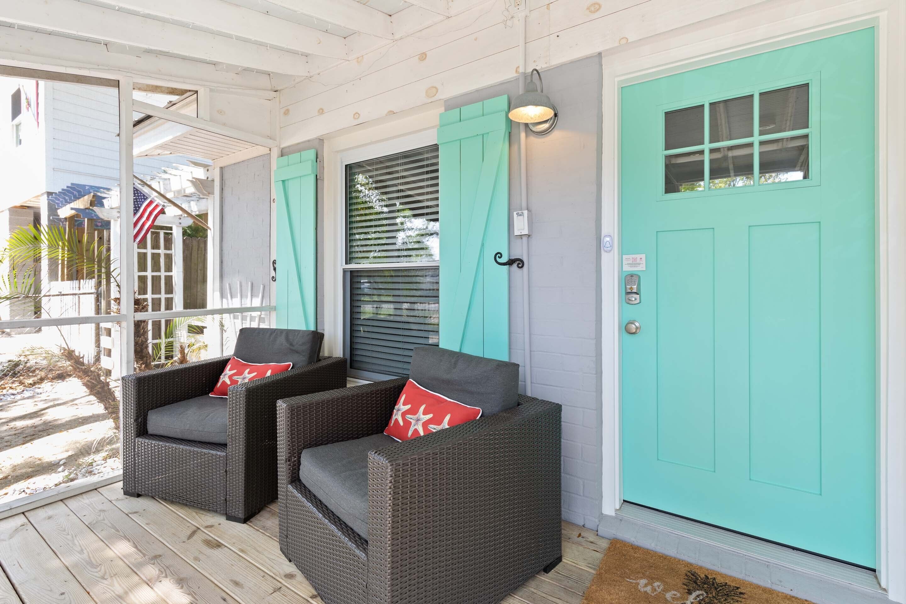 A porch with two wicker chairs, a teal door, and a small American flag.