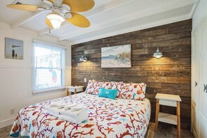 Ein Schlafzimmer mit einer Holzwand, einem Bett mit Blumenmuster, einem Deckenventilator und zwei Wandleuchten.