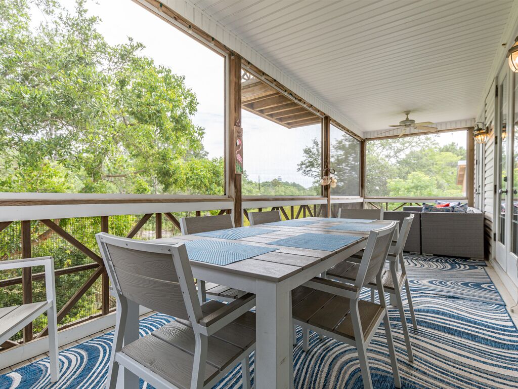 A covered outdoor area with a table and chairs, large windows, and a view of greenery.