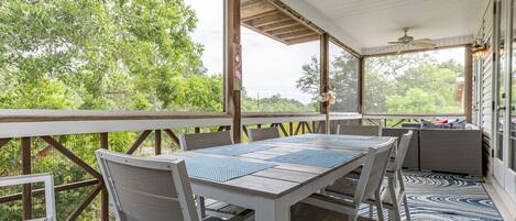 A covered outdoor area with a table and chairs, large windows, and a view of greenery.