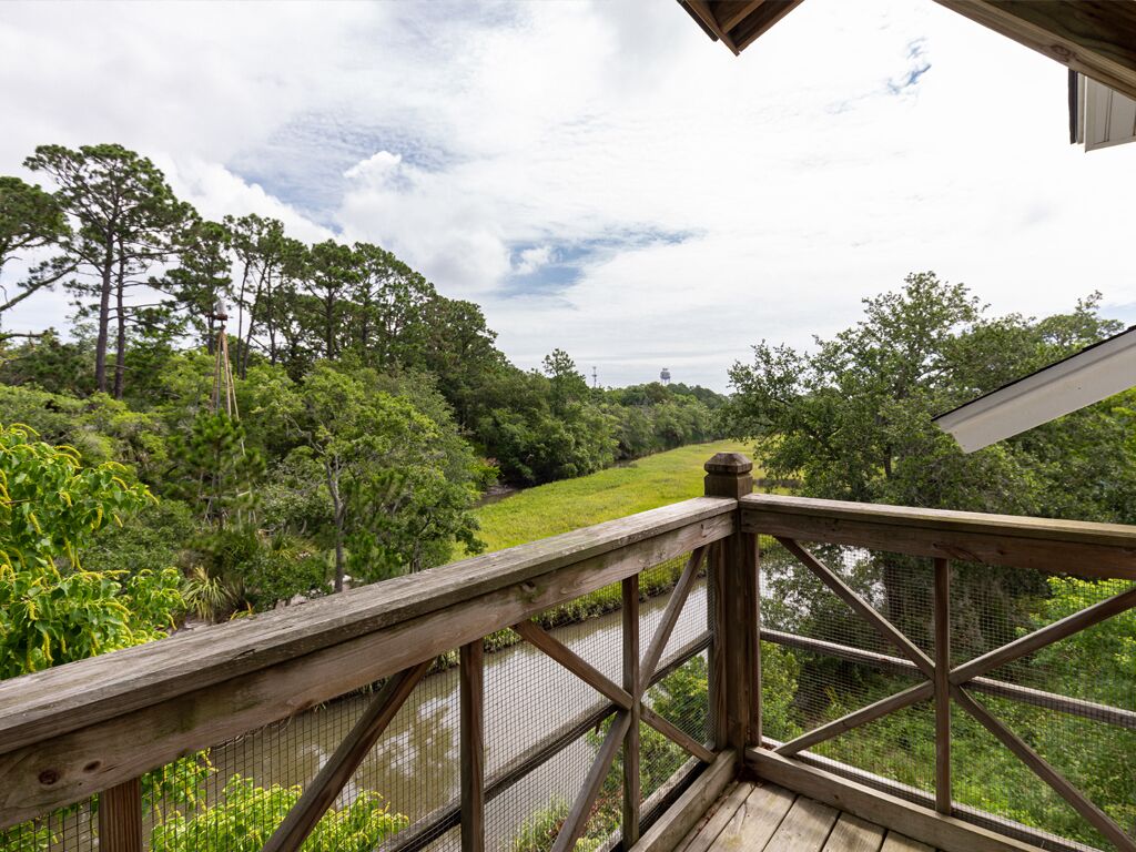 A wooden deck with a metal railing overlooking a lush green landscape and a body of water.