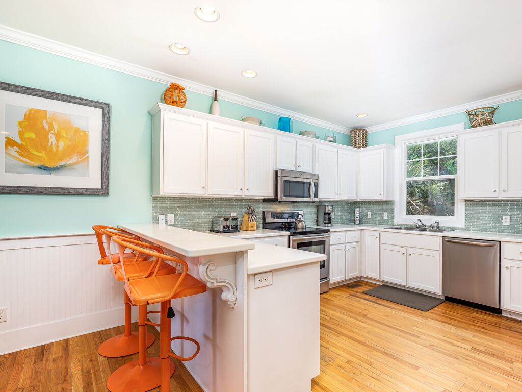 A modern kitchen with white cabinets, a central island with bar stools, a microwave, oven, and dishwasher.