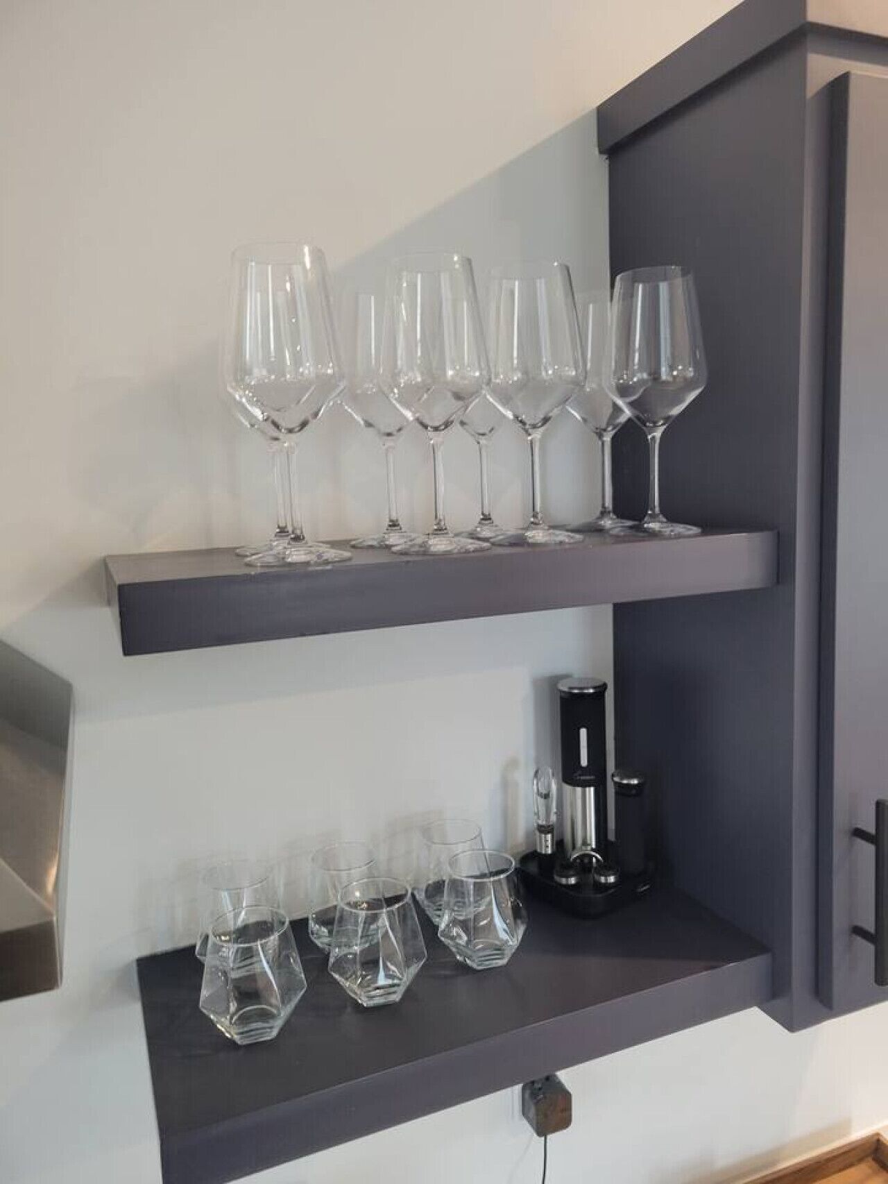 Una cucina con due ripiani: il ripiano superiore contiene bicchieri da vino e quello inferiore bicchieri per l'acqua e una macchina da caffè.