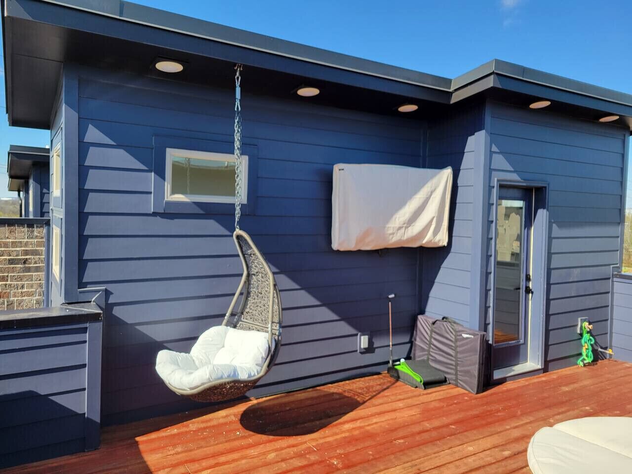 Ein blaues Gebäude mit einer Holzterrasse, einem Hängesessel, einer Tür und einem kleinen Fenster.