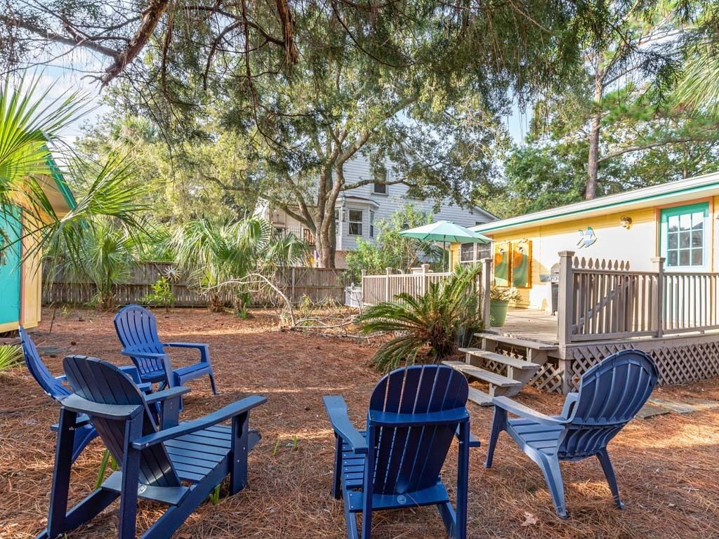 A backyard with Adirondack chairs, a wooden deck, and a house with a porch.