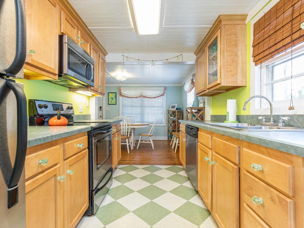 A kitchen with wooden cabinets, a microwave, stove, and a dishwasher. There is a window with blinds and a checkered floor.