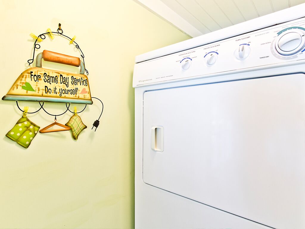 A white washing machine with control knobs and a wall-mounted laundry rack with clothes and a sign.