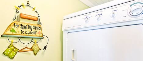A white washing machine with control knobs and a wall-mounted laundry rack with clothes and a sign.