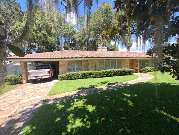 A house with a stone patio, a covered garage, and a well-maintained lawn. - Lakefront house for rent (Winter Haven)