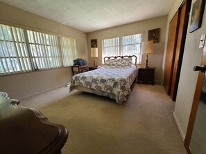 A bedroom with a bed, two bedside tables, a nightstand, a dresser, and a window with blinds.