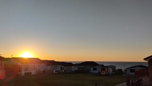 Une rangée de cabanes au bord de la plage, avec un coucher de soleil en arrière-plan.