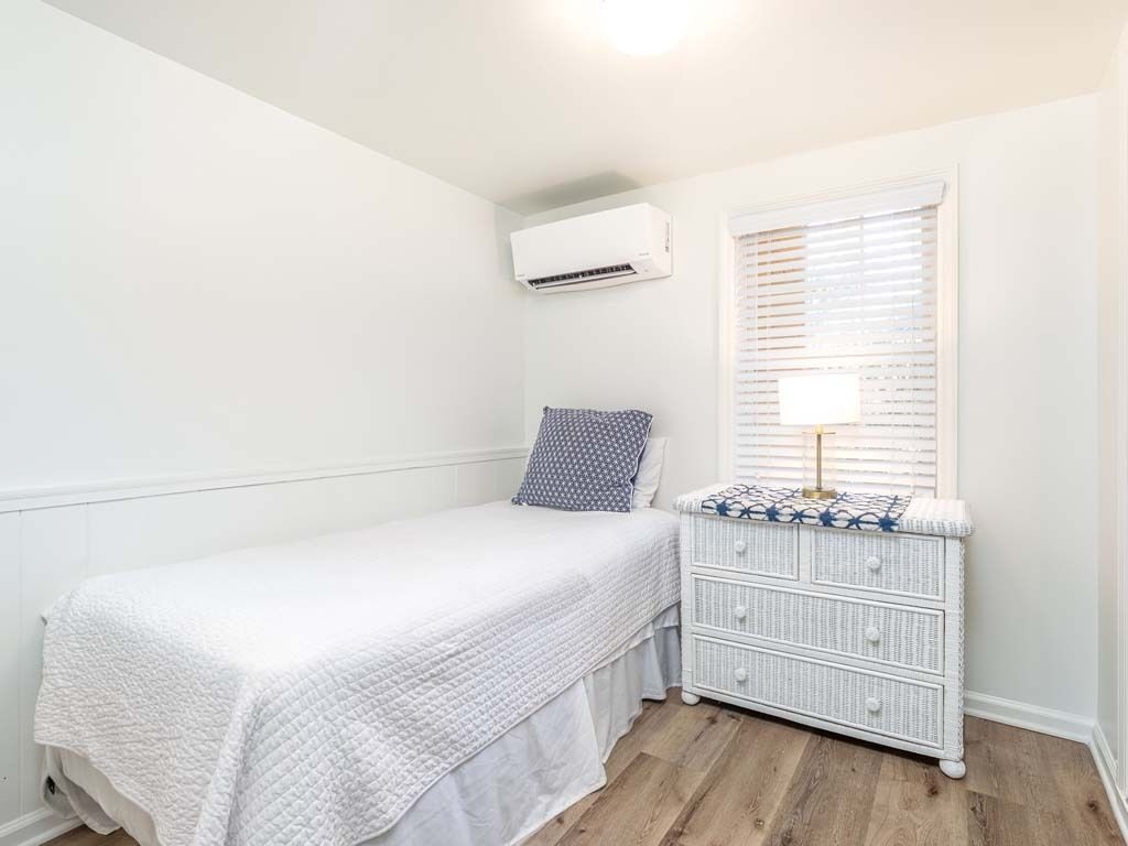 A small, neatly arranged bedroom with a single bed, a dresser, and an air conditioning unit on the wall.