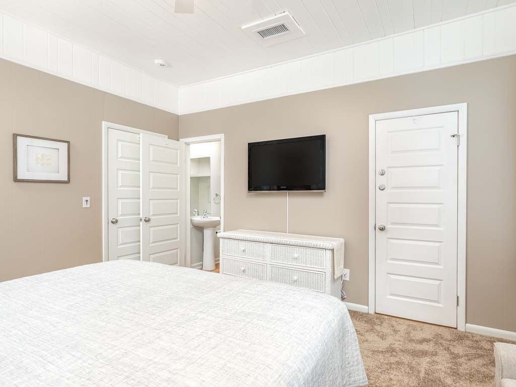 Een slaapkamer met een bed, een televisie, een witte dressoir en twee witte deuren.
