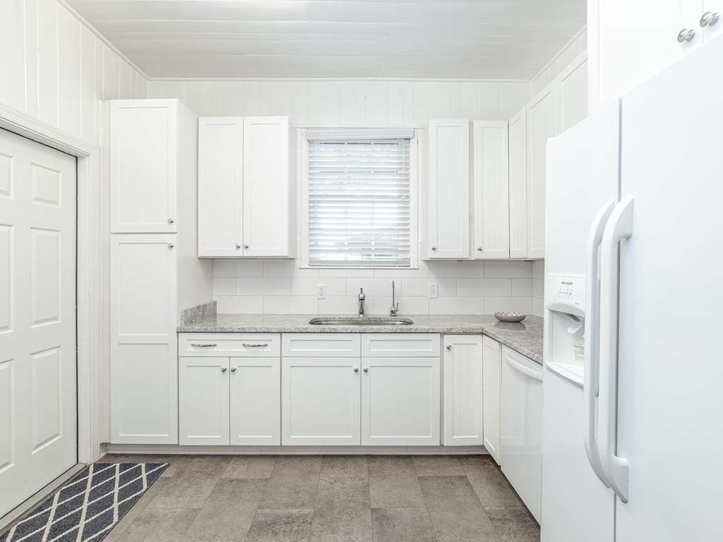 A compact kitchen with white cabinets, a granite countertop, a built-in sink, and a white refrigerator.