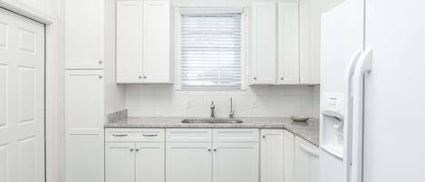 A compact kitchen with white cabinets, a granite countertop, a built-in sink, and a white refrigerator.