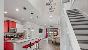 Une cuisine moderne avec des meubles de couleur rouge, un îlot central doté de tabourets de bar et un escalier menant à un deuxième étage.