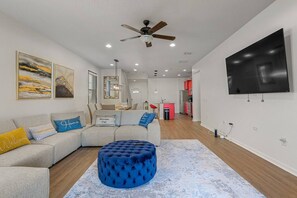 Un salon moderne avec un canapé d’angle, un pouf bleu et des œuvres d’art accrochées aux murs.