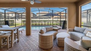 Une terrasse extérieure couverte avec une piscine, des meubles en osier et un ventilateur de plafond.