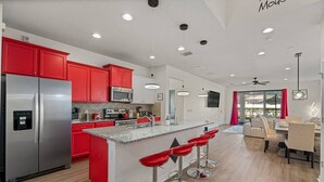 Une cuisine moderne avec des meubles de rangement rouges, des appareils en acier inoxydable et un îlot central doté de tabourets de bar.