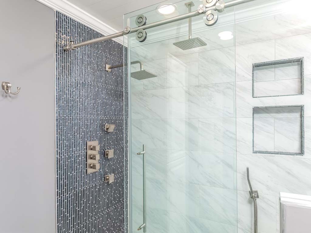 A modern bathroom with a glass shower enclosure, a tiled wall, and a marble floor.