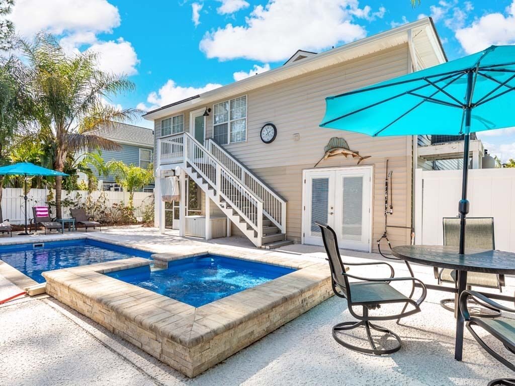 A pool area with a staircase leading to a deck, outdoor seating, and a covered patio.