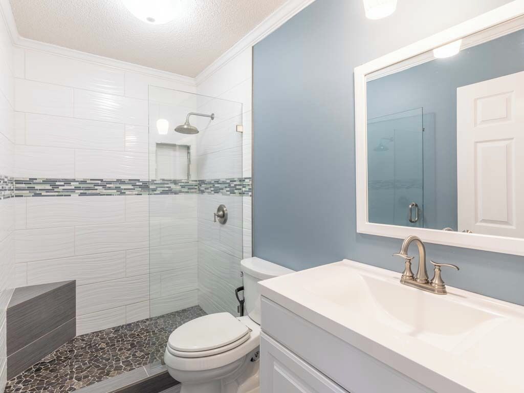 A bathroom with a white toilet, a glass shower enclosure, a white sink with a mirror, and a tiled floor with a mix of white and dark tiles.