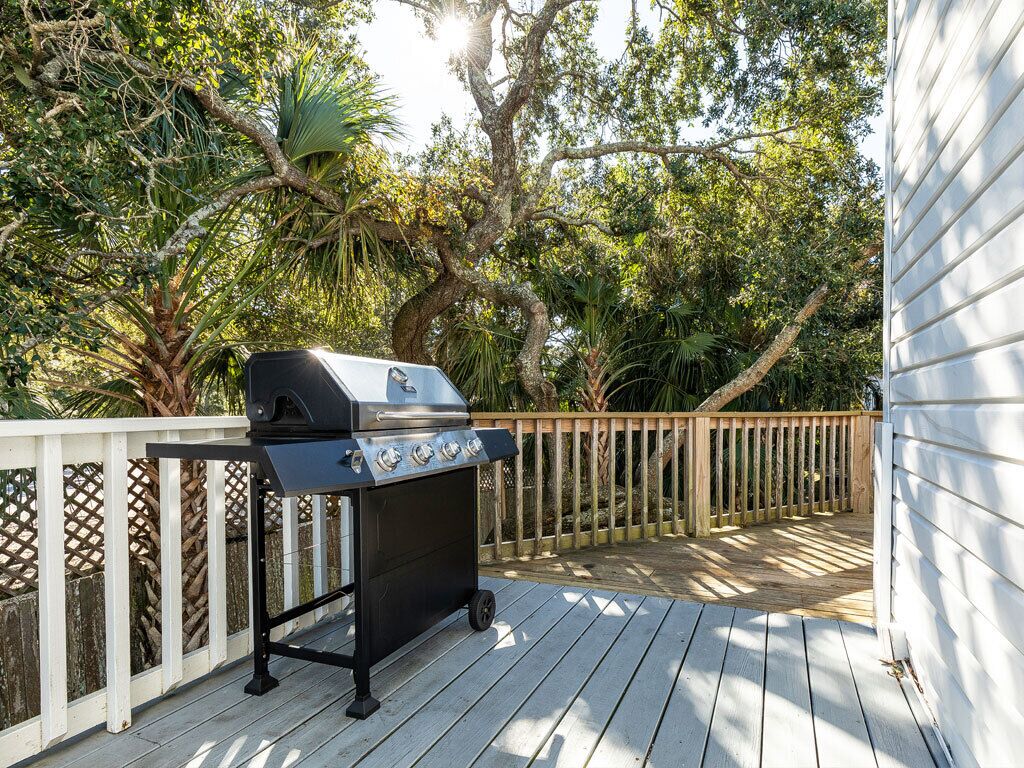 A barbecue grill on a wooden deck with a white fence and lush greenery in the background.