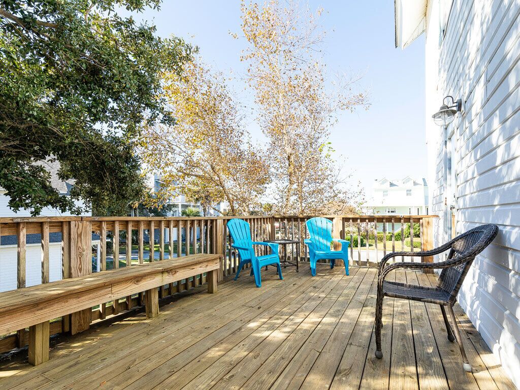 Een houten terras met een leuning, twee blauwe Adirondack-stoelen en een rieten stoel.