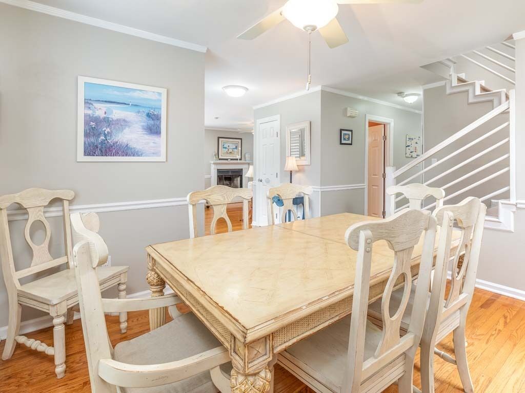 A dining area with a wooden table and chairs, a ceiling fan, and a staircase leading to another room.