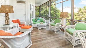 A covered porch with wicker furniture, a ceiling fan, and large windows offering a view of the outdoors. - Ocean Oasis by Tybee Vacation Rentals (Tybee Island)