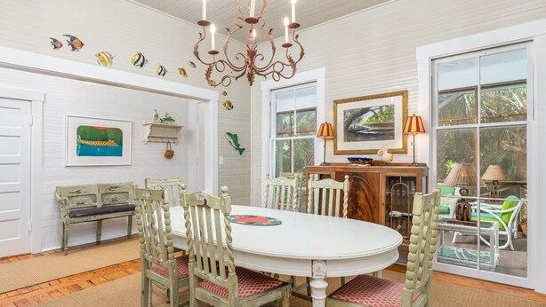 A dining area with a white oval table, four chairs, a chandelier, and a view through a glass door. - Ocean Oasis by Tybee Vacation Rentals (Tybee Island)