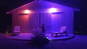 Ein modernes Haus mit einer überdachten Terrasse, ausgestattet mit zwei weißen Adirondack-Stühlen und einem kleinen Tisch.