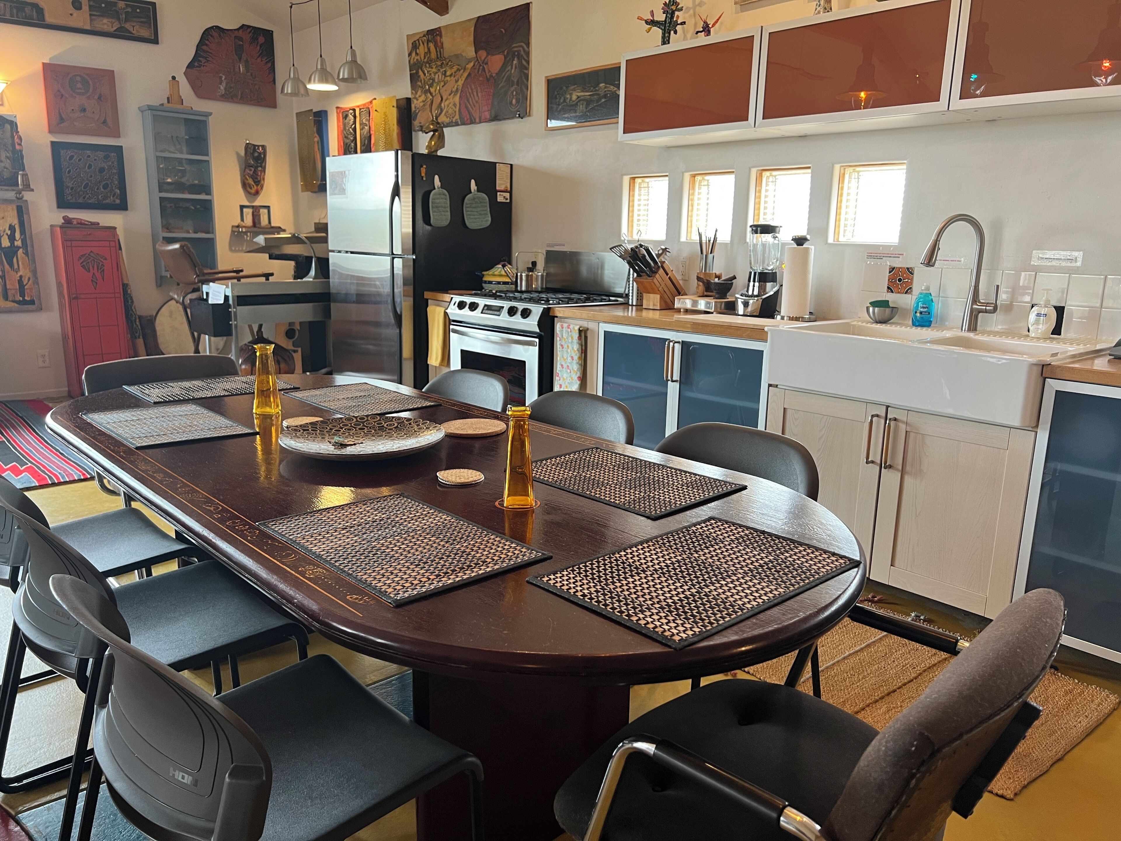 A modern kitchen with a dining area, featuring a long wooden table, black chairs, and a built-in oven.