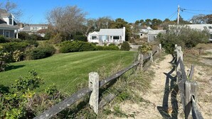 A residential area with a well-maintained lawn, a wooden fence, and houses in the background. - Cozy Oceanview 1BR Cottage Across from the Beach! (Harwich)