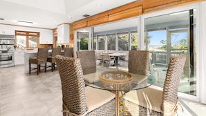Une cuisine moderne avec des meubles blancs, un coin repas avec des chaises en osier et de grandes portes-fenêtres coulissantes donnant sur un balcon.