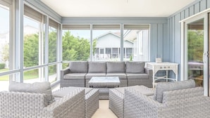 Une véranda meublée de mobilier en osier, dotée de grandes fenêtres et offrant une vue sur une maison.