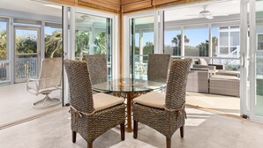 Un espace repas entièrement vitré, avec des chaises en osier et une table en verre, donnant sur un balcon aménagé avec du mobilier d’extérieur.