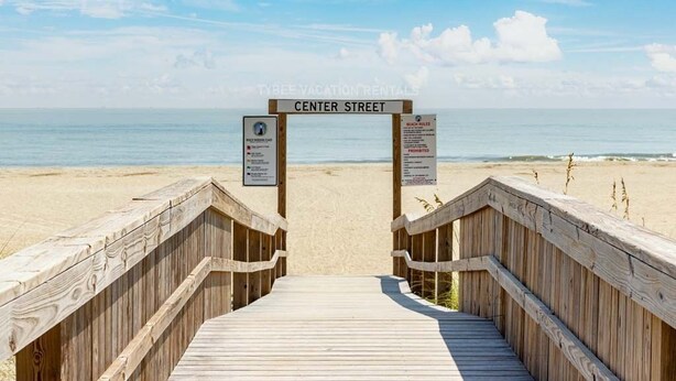 A wooden boardwalk leading to a beach with a sign reading 'CENTER STREET' and two informational signs on either side.