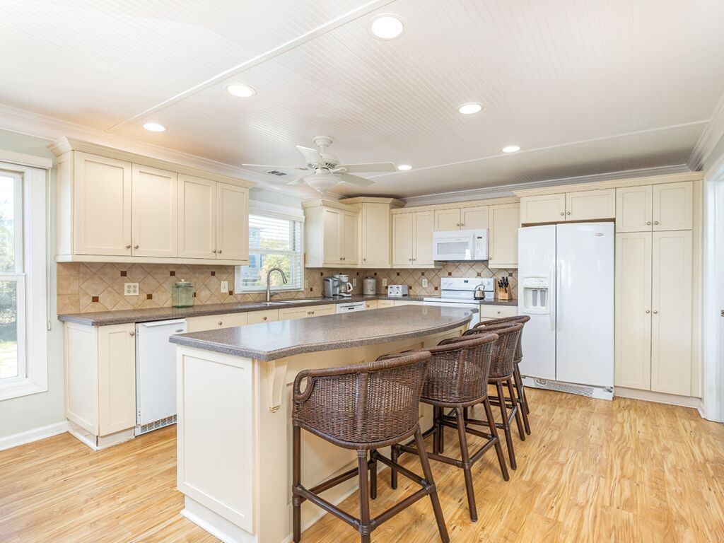 A spacious kitchen with a central island, white cabinets, and a wooden floor.