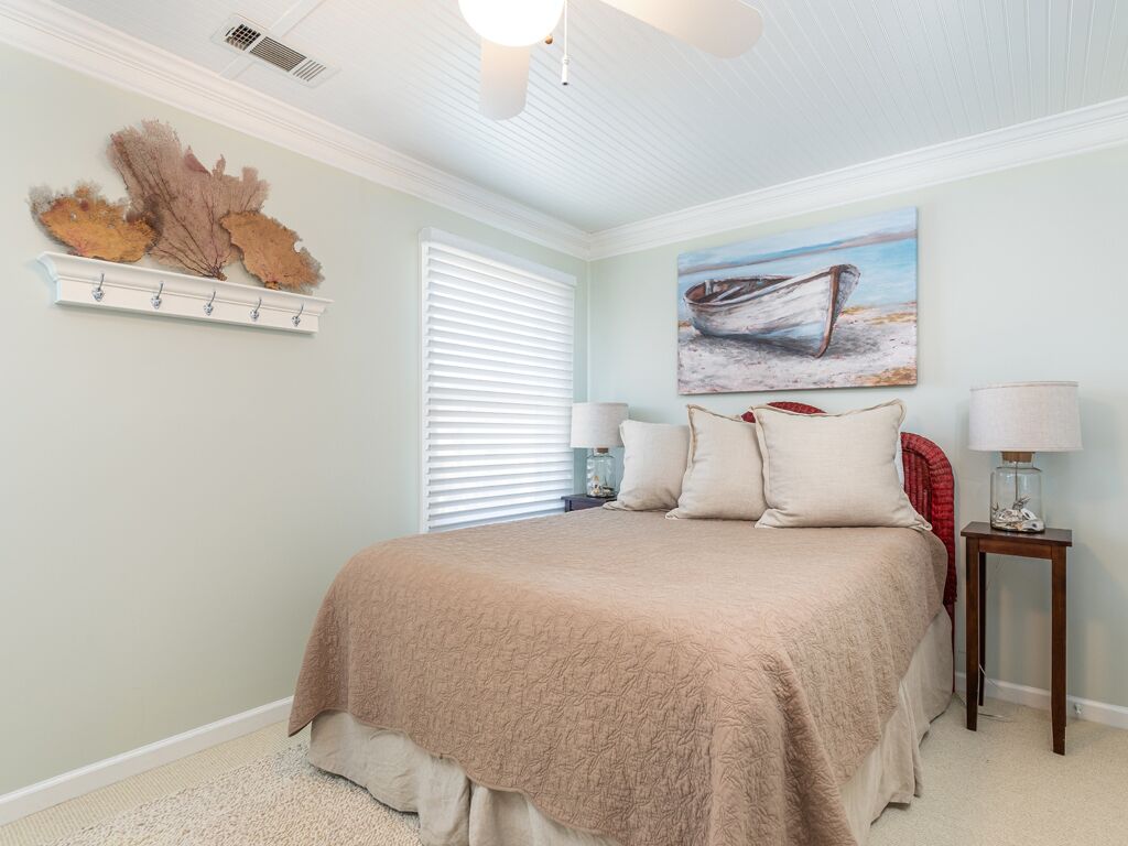 A bedroom with a large bed, a painting of a boat on the wall, and a shelf with decorative items.