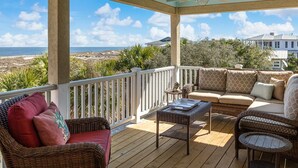 A covered outdoor deck with wicker furniture, a ceiling fan, and a view of the ocean.